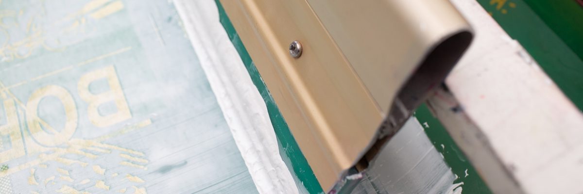 Serigraphy silk screen print process at clothes factory. Frame, squeegee and plastisol color paints.